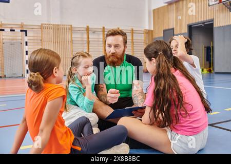 Ein männlicher Lehrer sitzt auf dem Boden, umgeben von einer Gruppe von Kindern in einem hellen und lebhaften Klassenzimmer. Stockfoto