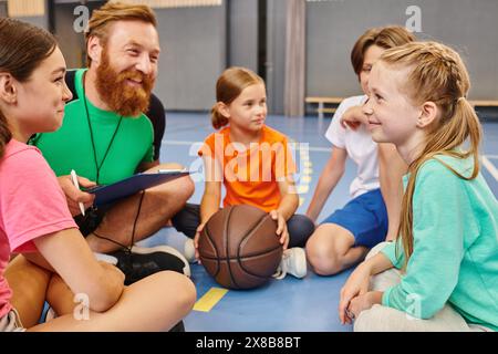 Eine vielfältige Gruppe von Kindern sitzt aufmerksam um einen Basketball herum, während ihr männlicher Lehrer sie in einem hellen, lebendigen Klassenzimmer unterrichtet. Stockfoto