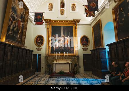 Malta Kapelle: Altar mit Malerei, Besucher beobachten Kunstwerke, umgeben von weiteren Gemälden und Holzschränken in der St. John's Co-Cathedral, Malta Stockfoto