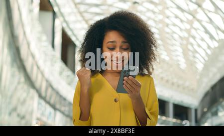 Glückliche afroamerikanische Frau freut sich Freude Handy Smartphone Handy Handy Handy ja aufgeregt emotionale Käufer Shopping Mall Verkäufe Rabatte schwarz Stockfoto
