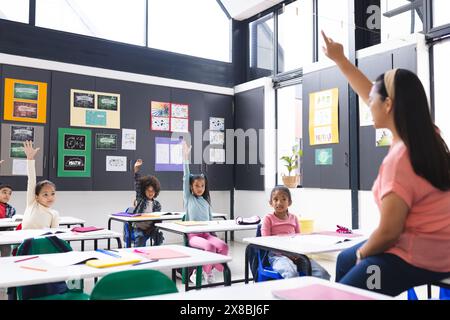 In der Schule engagieren sich junge, birassische Lehrerin mit verschiedenen Schülern im Klassenzimmer Stockfoto