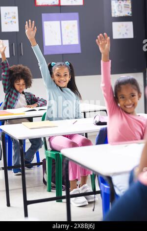 In der Schule gab es eine vielfältige Familie mit zwei jungen Töchtern und einem Sohn, der im Klassenzimmer die Hände hebt Stockfoto