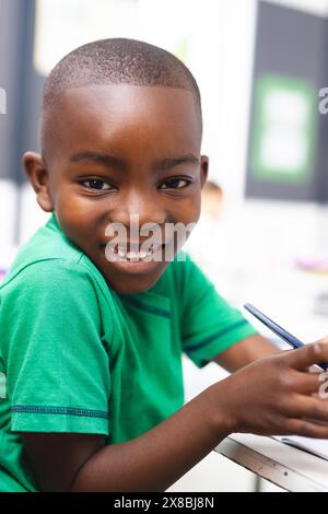 In der Schule schreibt ein junger afroamerikanischer Junge, der ein grünes Hemd trägt, im Klassenzimmer Stockfoto