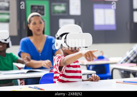 In der Schule, im Klassenzimmer, beobachtet birassische Lehrerin die Schüler, die VR-Headsets tragen Stockfoto