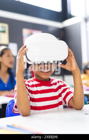 In der Schule lächelt ein junger afroamerikanischer Junge, der ein VR-Headset trägt, im Klassenzimmer Stockfoto