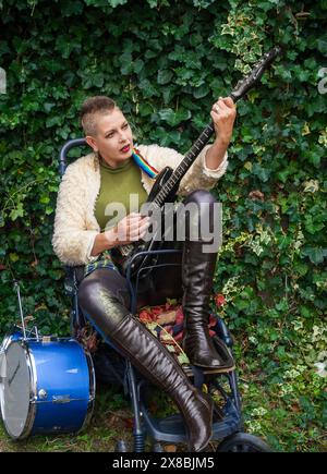 Punkig aussehende Frau, die Gitarre in einem alten Kinderwagen spielt Stockfoto