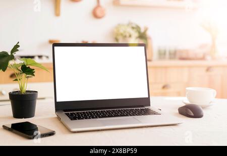 Ein Arbeitsplatz in einer hellen Küche während der Quarantäne. Laptop mit Platz für Text. Telearbeit. Freiberuflich. Blumentopf, Telefon und Tasse auf dem Tisch. Stockfoto