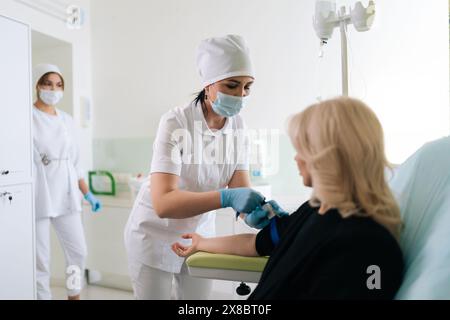 Fachlabor in Uniform mit Tourniquet am Arm einer Patientin vor intravenöser Therapie auf der medizinischen Station. Prozess der Verwaltung Stockfoto