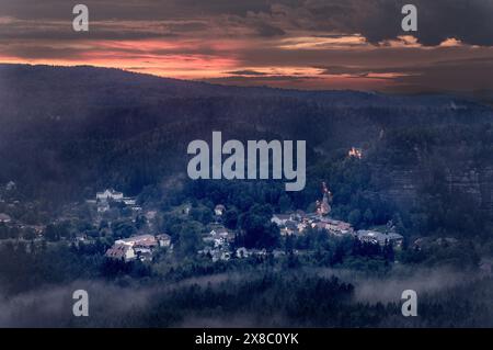Nebel weht bergauf durch das Tal zu den Bergen. Die historische Burgruine und die barocke Bergkirche sind über dem Kurort Oybin zu sehen. Stockfoto