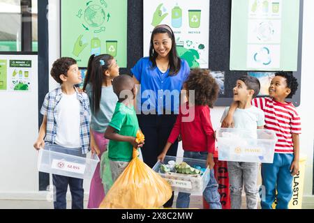 In der Schule, Lehrer für ethnische Rasse mittleren Alters und junge Schüler, die Recyclingbehälter im Klassenzimmer halten Stockfoto