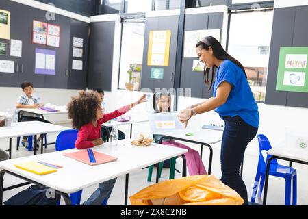 In der Schule recycelt der birassische Lehrer mittleren Alters mit verschiedenen Schülern im Klassenzimmer Stockfoto