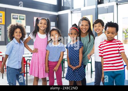 In der Schule lächelt eine birassische Lehrerin mittleren Alters mit ihren jungen Schülern im Klassenzimmer Stockfoto