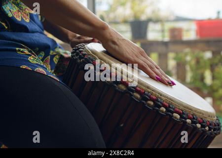 Nahaufnahme weiblicher Hände auf dem ledernen Kopf einer Djembe-Trommel einer unerkennbaren Frau zu Hause. Nahaufnahme Seitenansicht einer Frau, die spielt, eine übt Stockfoto