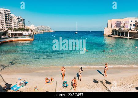 Schwimmer und Sonnenanbeter entspannen sich im flachen türkisfarbenen Wasser am ruhigen Balluta Bay Beach in St. Julian's, Malta Stockfoto