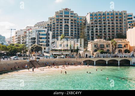 Die Menschen entspannen sich im flachen türkisfarbenen Wasser am wunderschönen Balluta Bay Beach in St. Julian's, Malta Stockfoto