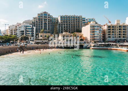 Schwimmer und Sonnenanbeter entspannen sich im flachen türkisfarbenen Wasser am atemberaubenden Balluta Bay Beach in St. Julian's, Malta Stockfoto