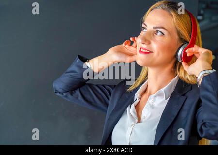 Glückliche Geschäftsfrau, die im Büro Musik mit Kopfhörern hört Stockfoto