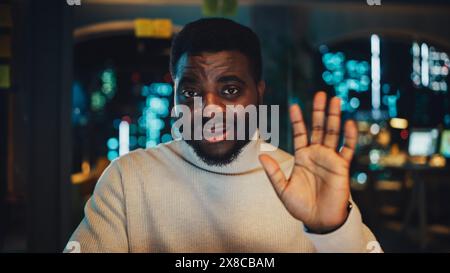 Blickwinkel aus der Kamera mit dem gutaussehenden Young Black Project Manager, der in einer abendlichen Büroumgebung ein Videogespräch führt. Afroamerikanischer männlicher Spezialist, der mit einem Kollegen über eine Live-Kamera spricht. Stockfoto