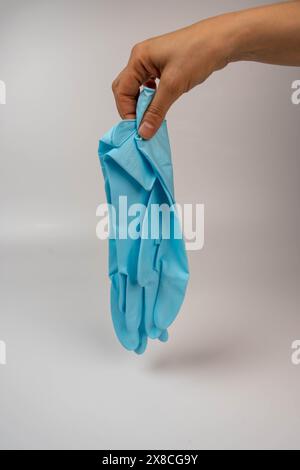 Eine Person, die einen blauen Nitrilhandschuh auf einer weißen Oberfläche hält. Stockfoto