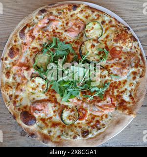 Pizza mit Rucola, Zucchini, Mini-Tomaten, Käse und Lachs Stockfoto