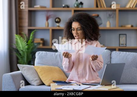 Verärgerte und verärgerte Frau, die zu Hause mit Dokumenten und Papieren arbeitet, Stromrechnungen und Kreditzahlungen bezahlt, schockiert durch hohe Zinsen für Versicherungen und Hypotheken. Stockfoto