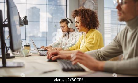 Porträt einer birazialen kreativen jungen Frau, die am Computer in einem hellen, beschäftigten Büro arbeitet. Weibliche Führungskraft Lächelt, Hat Einen Produktiven Tag. Menschen, die im Hintergrund arbeiten. Stockfoto