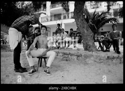 Mallorca Mallorca Spanien 1987 Port de Pollenca, Puerto Pollensa Haarschnitt am Strand Port de Pollensa oder „Puerto Pollensa“, wie es manchmal geschrieben wird, ist ein Resort, das besonders bei den Briten beliebt ist – für Ferien und als Zweitwohnsitz – und bietet gute Einrichtungen, Strände und ausgezeichnete Möglichkeiten für Wassersport. Mallorca, oder Mallorca, ist die größte Insel der Balearen, die Teil Spaniens sind, und die siebtgrößte Insel im Mittelmeer. Die Hauptstadt der Insel, Palma, ist auch die Hauptstadt der autonomen Gemeinschaft der Balearen. Die Balearen Sind Stockfoto