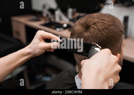 Der Kunde bekommt seine Haare mit einem elektrischen Trimmer vom Friseur in einem Friseur rasiert. Stockfoto