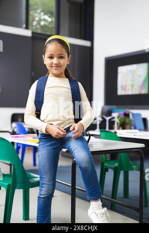 In der Schule stand ein junges birassisches Mädchen im Klassenzimmer und trug einen Rucksack Stockfoto