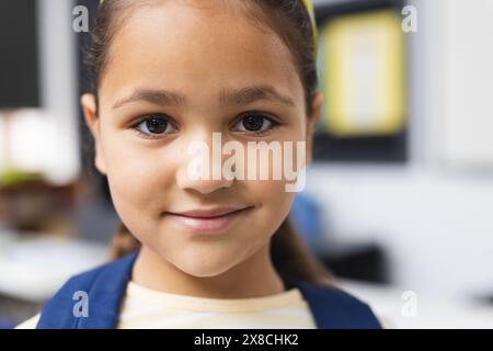 In der Schule lächelt ein junges birassisches Mädchen mit hellbrauner Haut im Klassenzimmer Stockfoto