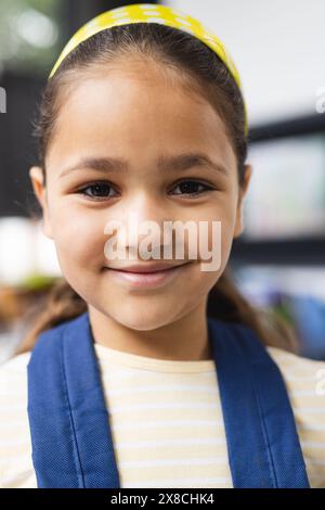 In der Schule, im Klassenzimmer, ein birassisches junges Mädchen, das eine blaue Weste trägt und lächelt Stockfoto