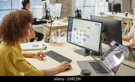 Porträt einer jungen birassischen Frau, die einen Computer in einem beschäftigten Executive Assistant benutzt, der an der Planung von Meetings arbeitet. Stockfoto