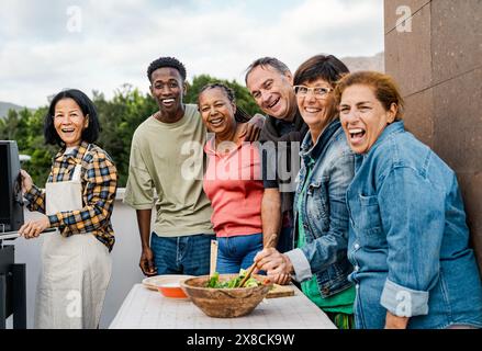 Glückliche, generationsübergreifende Freunde, die Spaß bei der Zubereitung von Speisen auf dem Dach des Hauses haben - Diversity People Lifestyle Stockfoto