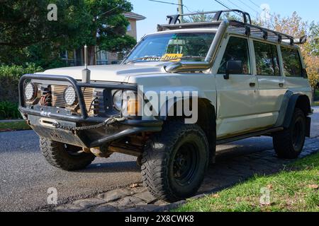 Der weiße Y60 Nissan Patrol 4x4 parkt in einer Vorstadtstraße, modifiziert für den Geländeeinsatz und mit verschiedenen Zubehörteilen an einem sonnigen Tag Stockfoto