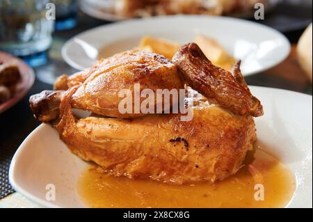 Das Bild zeigt ein geröstetes Huhn, das auf einer weißen Tafel sitzt. Das Huhn ist goldbraun und knusprig. Die Säfte laufen vom Huhn. Th Stockfoto