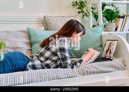 Eine Schülerin, die zu Hause mit einem Laptop liegt und Videounterricht hat Stockfoto
