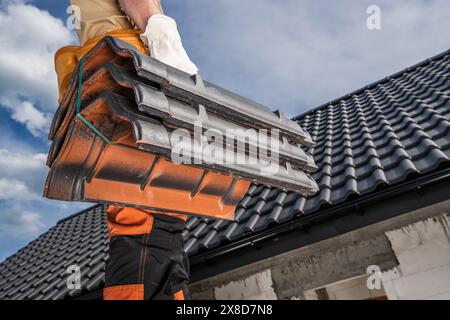 Der kaukasische Dachdecker steht auf einem Dach und hält Keramikziegel. Stockfoto