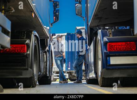 Zwei Trucker stehen vor einem großen Sattelzug. Der eine hält ein Klemmbrett und der andere sieht den Lkw-Motor an. Das Fahrzeug ist p Stockfoto