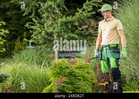 Ein Mann mit grüner Hose und Hut steht inmitten üppiger Grünflächen in einem Garten. Stockfoto