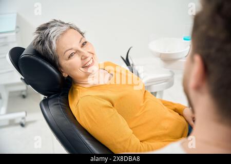 Frau Klientin in ihrem 50, die einen Arzt Stomatologen ansieht und lächelt Stockfoto