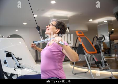 Frau mittleren Alters, die Sportkleidung trägt und Sport für den Rücken im Fitnessstudio macht Stockfoto
