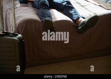 Abgeschnittenes Bild eines müden männlichen Unternehmers, der auf dem Bett im Hotelzimmer liegt und ruht Stockfoto