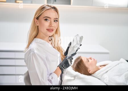 Kosmetologe hält Laser-Haarentfernungsmaschine in der Nähe einer verschwommenen jungen Frau Stockfoto