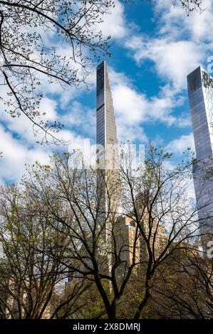 NYC's Art déco-Juwel sonnt sich! Der Steinway Tower erhebt sich an einem sonnigen Tag über üppiges Grün im Central Park und einige Bäume im Vordergrund. Stockfoto