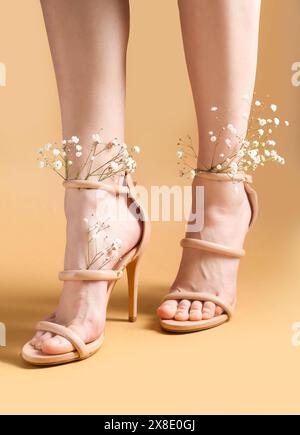 Beine der schönen jungen Frau in beigen Knöchelriemen Schuhe mit weißen gypsophila Blumen auf beigem Hintergrund Stockfoto