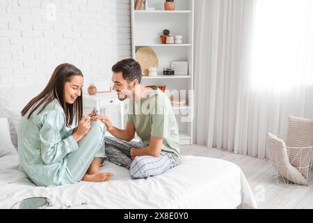 Junger Mann, der nagellack von seiner Frau im Schlafzimmer bekommt Stockfoto