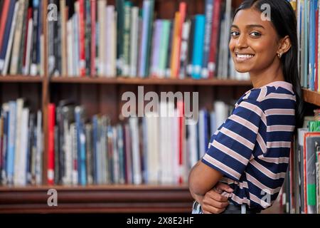 Indische Frau, Studentin und Porträt in der Universitätsbibliothek zum Lesen von Büchern oder zur Projektforschung, zum Entspannen oder zum Lernen. Weibliche Person, Gesicht und Lächeln weiter Stockfoto