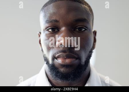 Im modernen Büro blickt ein junger Afroamerikaner mit kurzen Haaren und Bart nach vorne. Mit weißem Hemd und ernsthaftem Gesichtsausdruck, s Stockfoto
