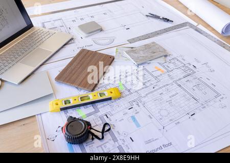 Architekturpläne und -Tools verteilen sich auf dem Schreibtisch und zeigen detaillierte Gebäudelayouts Stockfoto