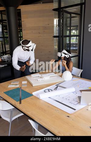 Junges, vielfältiges Team im Büro, das VR-Headsets verwendet und mit virtuellen Modellen interagiert. Afroamerikaner in weißem Hemd und indische Frau in schwarzen Dres Stockfoto